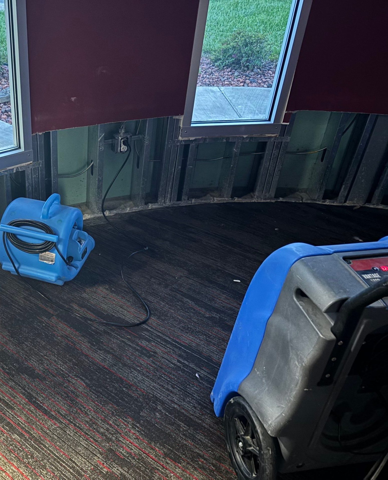 Air mover and dehumidifier drying a wall after water-damaged drywall removal