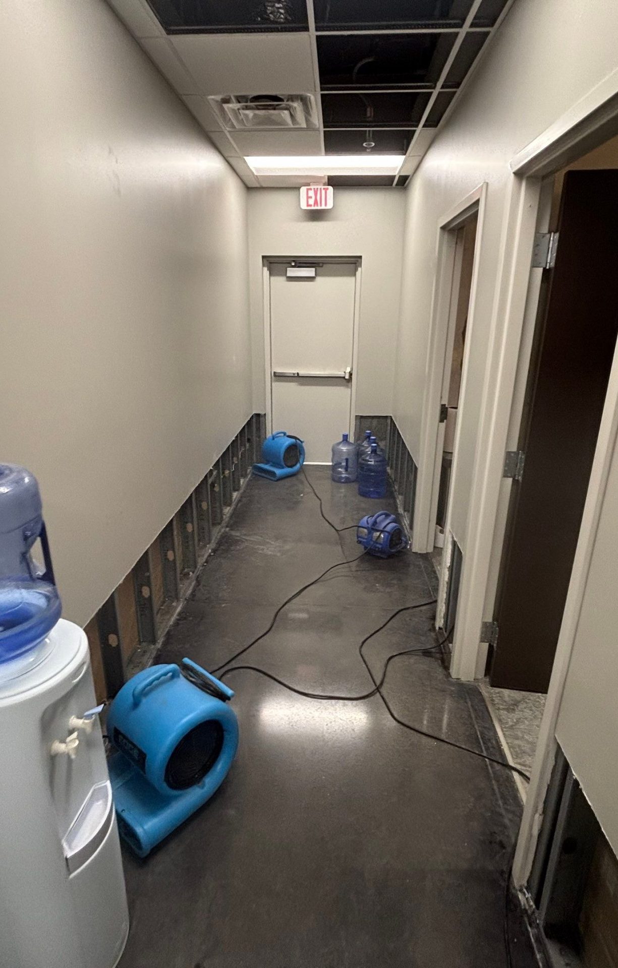 Hallway with water-damaged drywall removed and fans drying exposed walls
