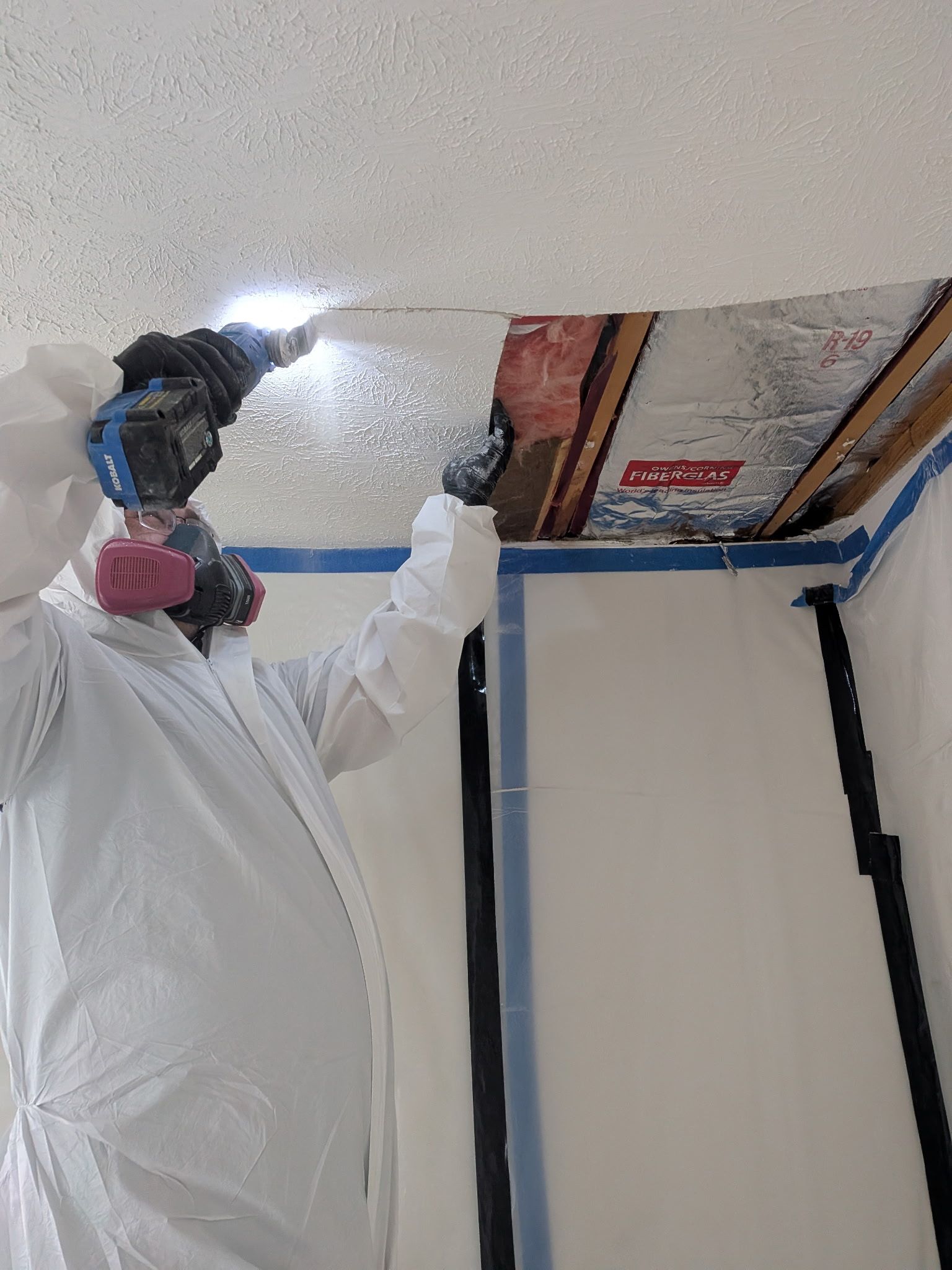 C2G Environmental technician wearing protective coveralls and a respirator using a power tool to remove ceiling material during residential asbestos abatement.