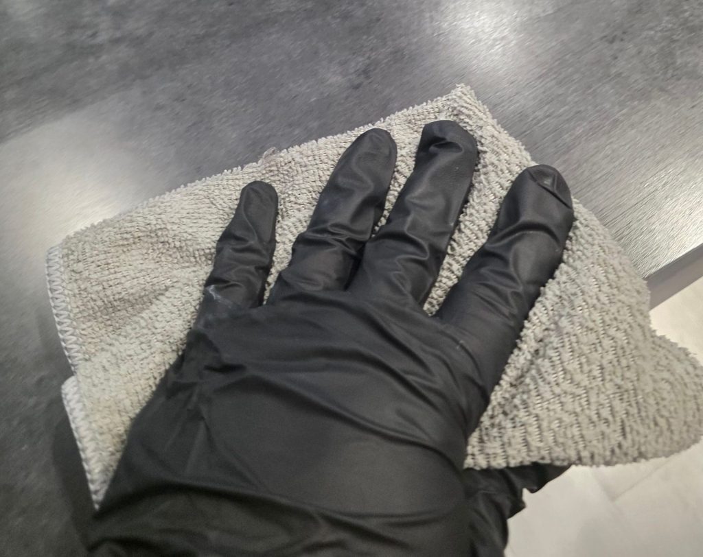 C2G Environmental technician wearing black protective gloves wiping a commercial countertop with a microfiber cloth during professional surface cleaning.