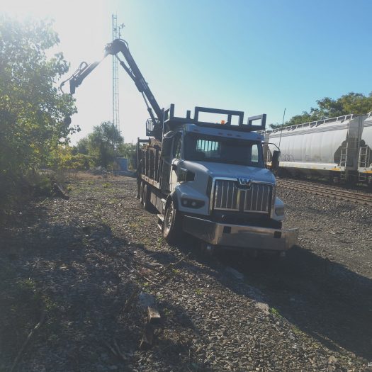 C2G grapple truck working beside railroad tracks and freight cars