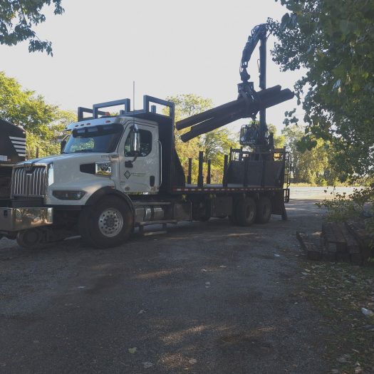 C2G hi-rail grapple truck handling railroad ties beside a locomotive