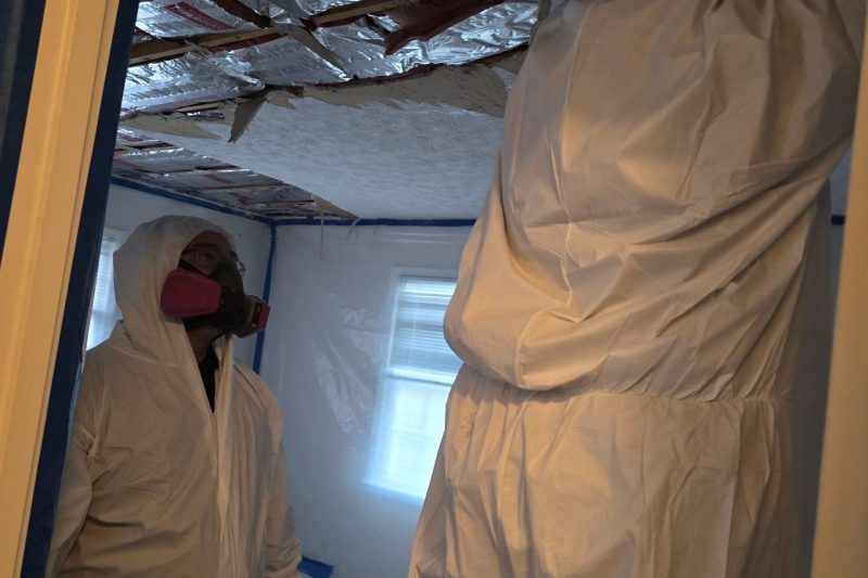 C2G Environmental technicians wearing protective suits and respirators performing ceiling demolition inside a contained asbestos abatement work area.