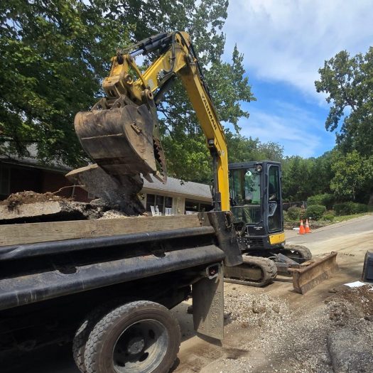 Excavator loading soil and concrete into a dump truck during site cleanup